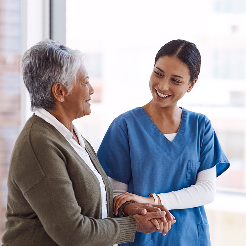 Nurse and resident walking arm in arm and smiling at each other